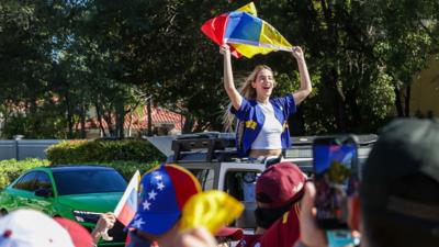 A woman waving a Venezuelan flag with her upper body sticking out on a car.