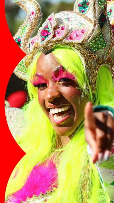 A Notting Hill Carnival performer with a colourful sparkling crown, elaborate pink eye lashes, and a luminous green wig 