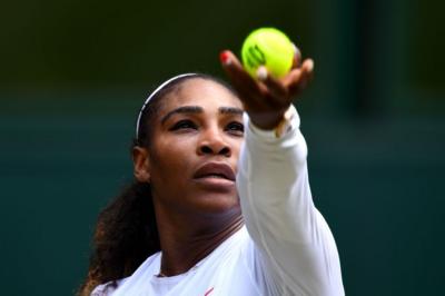 Serena Williams holds a tennis ball above her head