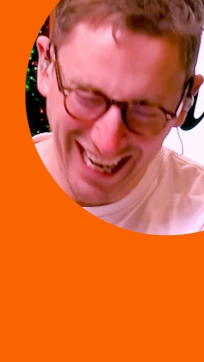 A close up of podcast host and comedian John Robins bent over laughing