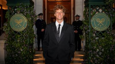 Jannik Sinner poses in a black suit at Wimbledon - he has short curly brown hair
