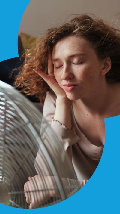 Woman with closed eyes sits in front of a fan as her hair is blown around.