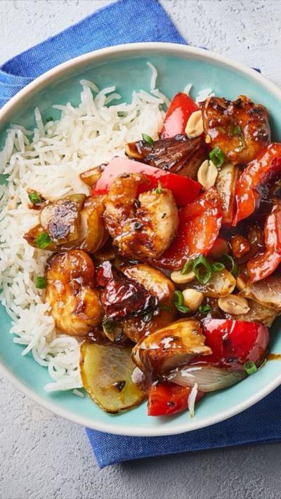 A blue bowl containing kung pao prawns, stir fried vegetables and white rice