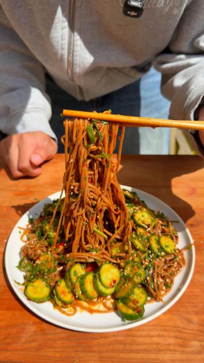 Smashed cucumber noodle salad on a plate with noodles being lifted up using chopsticks 