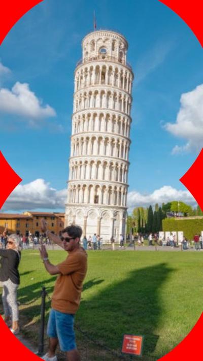 A man wearing an orange T-shirt and blue shorts is stood in front of the Leaning Tower of Pisa, with his hands raised up pretending to hold it from falling.