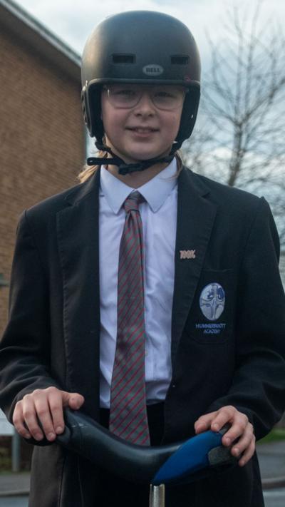 Alfie wearing a black blazer over a white shirt with red striped tie. Picture in picture shows him riding a unicycle.