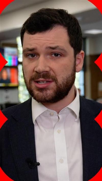 Henry Zeffman in BBC newsroom. He wears a shirt and blazer and has a beard.