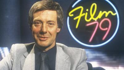 Barry Norman in front of a neon sign which reads 'Film 79'.