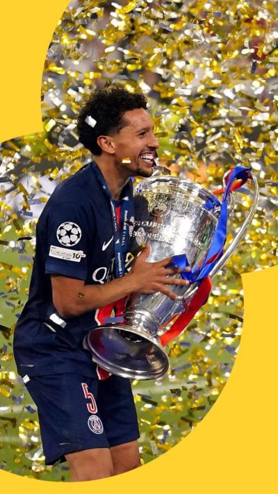 Marquinhos holding up trophy and smiling, yellow confetti around him