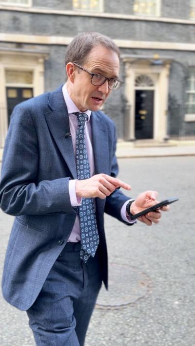 Chris Mason, wearing a blue suit, standing outside No 10 Downing street, pointing at his phone.