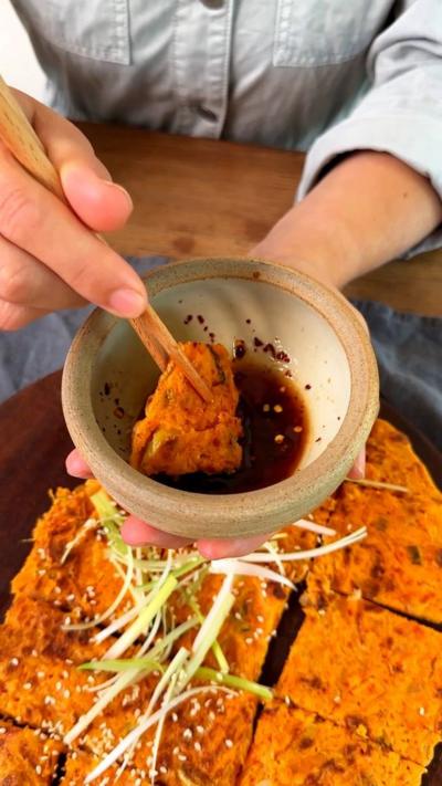 Somebody holding the Korean kimchi pancake with sticks and dipping it into sauce