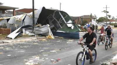 Residents from Sydney"s southern suburb of Kurnell cycle past the damaged homes