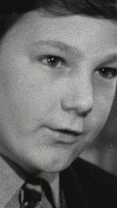 A young boy in black and white film wearing a school uniform.