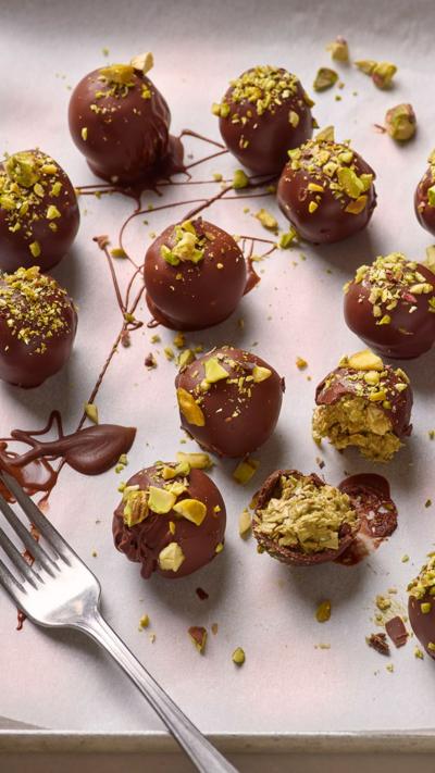 Lots of pistachio covered chocolate balls sit on a plate with a fork next to them