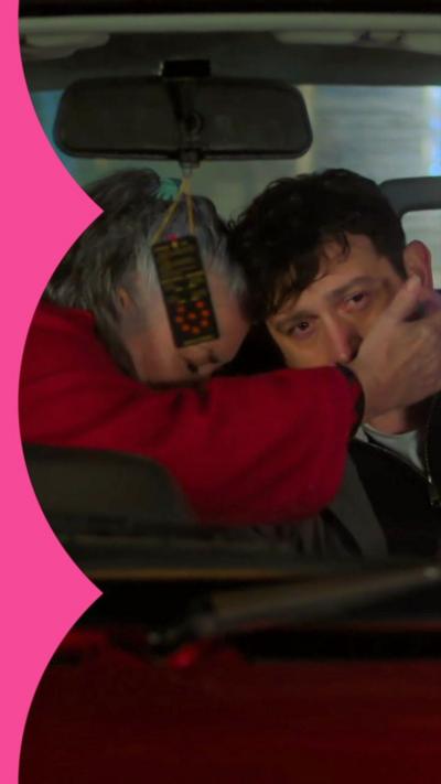 A woman hugs a man in the front of a car