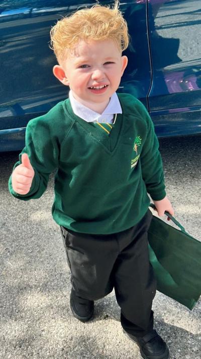 A young boy in a green school jumper with his thumb up