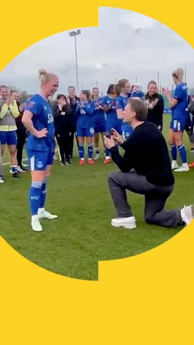 A woman, Everton footballer Rikke Madsen, wears her team's blue kit and holds her baby who wears a matching kit up in the air