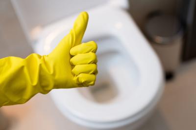 A hand in cleaning glove giving a thumbs up over a toilet
