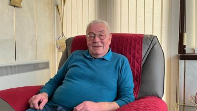 Murchadh MacIlleathain, a tha le aillse a' phròstata, na shuidhe le gàire air aodann.