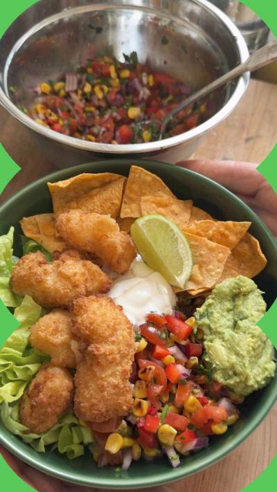 Two bowls, one silver one with salad inside and a green bowl of scampi, salad and tortilla chips.