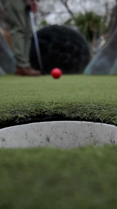 A red gold ball travelling towards a hole on the course.