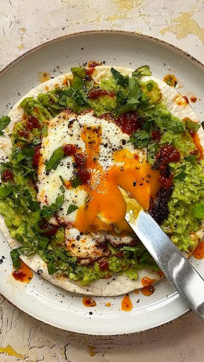 A taco topped with a fried egg, avocado and harrissa on a plate sat on a marble worktop