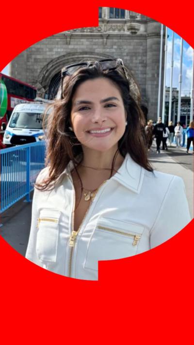 Valentina Gomez has long dark hair, is wearing a white jacket and black trousers, standing on Tower Bridge.