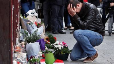 A man holds his head in his hands as he lays flowers