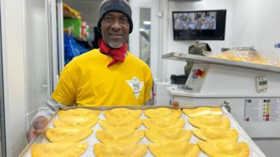 'Baker’ smiles as he holds up a tray of patties