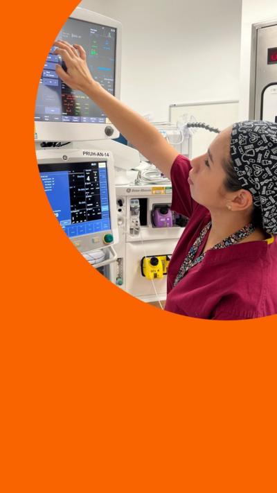 A woman dressed in red scrubs looks and points at medical equipment 