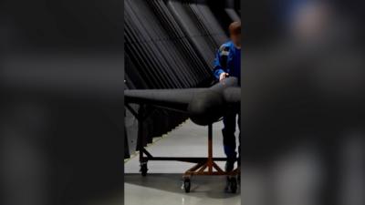 A still of the video, showing a man in blue uniform guiding a large black drone on wheels.