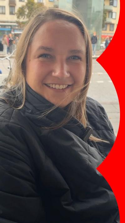 A woman smiles while sitting outside in a black coat