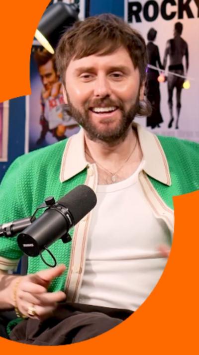 James Buckley has short hair and is wearing a green cardigan over a white top.