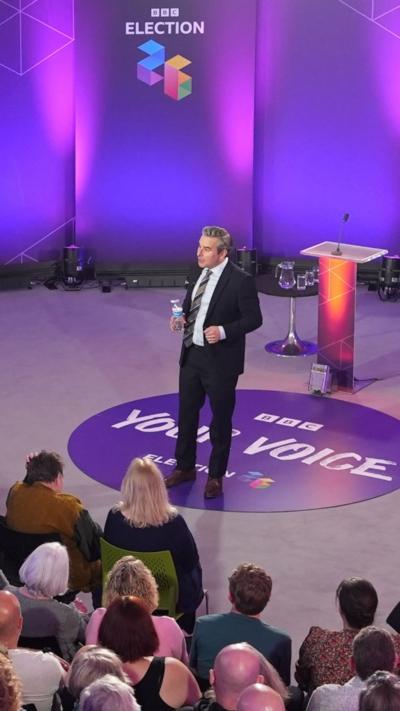 Nick Servini talking to the crowd in front of purple BBC Election 2026 branding