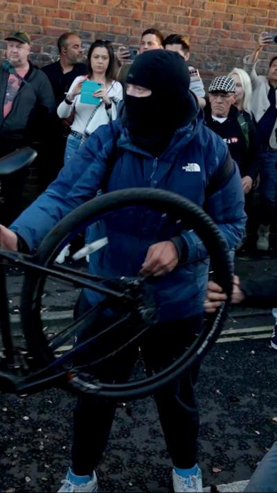 A man holding a bike and wearing a balaclava