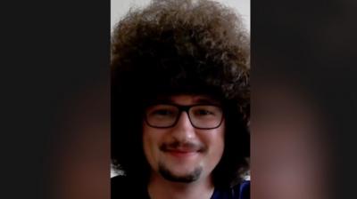Manchester United fan Frank Ilett has large curly dark hair, bigger than his face, and is wearing glasses