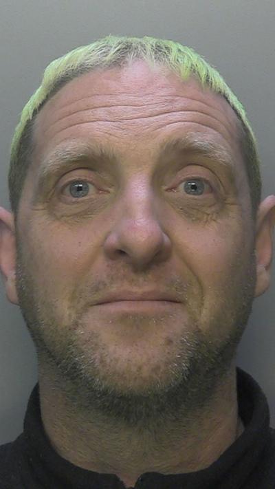 A police mugshot of a man with green hair.