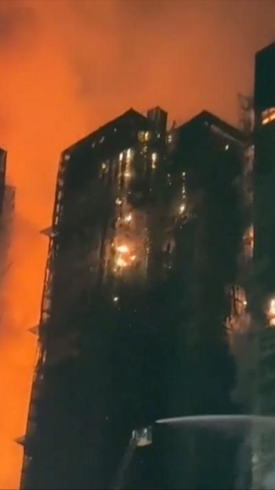 At night flames and bright red smoke engulf black tower blocks.