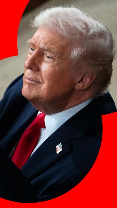 Donald Trump wears a dark blue suit jacket, white shirt and red tie, with a US flag pin badge 