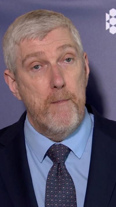 John O'Dowd in navy suit jacket, blyue shirt and purple tie