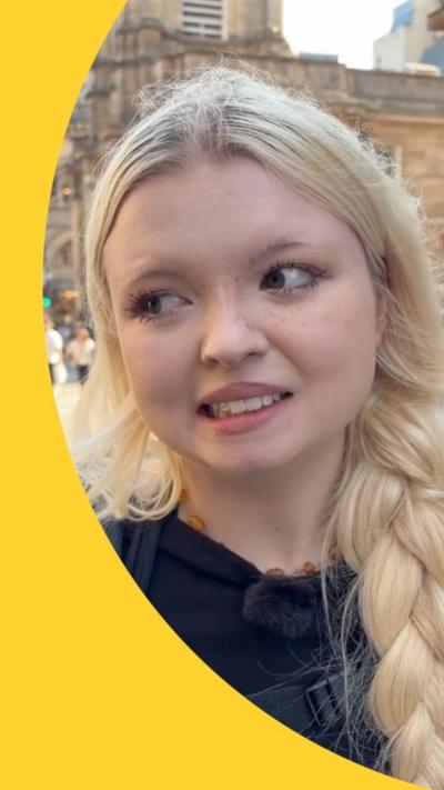 A woman with long, blonde hair in a side plait looks to one side