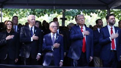 Five people are lined up side-by-side with their right hand to their chest.