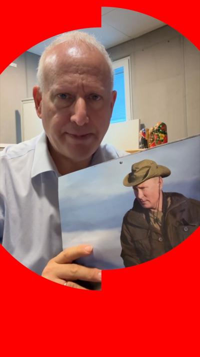 Steve Rosenberg holds a calendar featuring an image of Vladimir Putin wearing a green hat and brown jacket