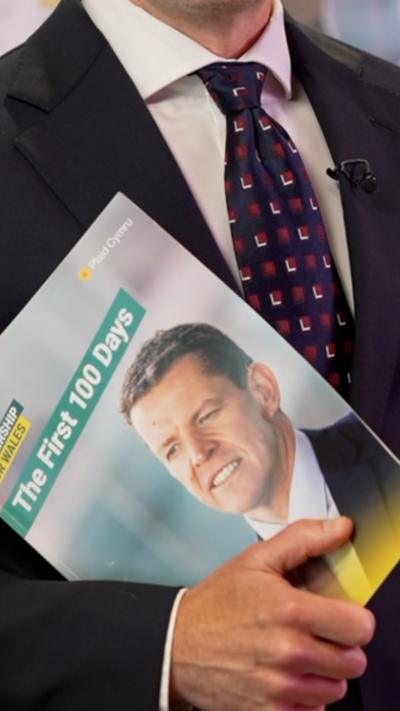 Someone in a suit holding a The First 100 Days manifesto with a picture of Rhun ap Iorwerth