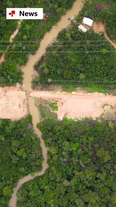 A drone shot of a road being dug through the green trees of the Amazon rainforest