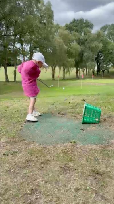 A small boy in a pink top playing golf. He is wearing a white baseball cap