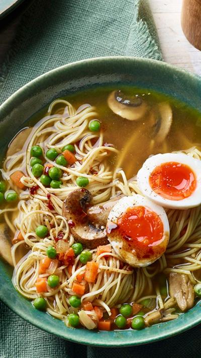 Top down view of a green bowl with mushroom ramen in. A small bowl of chilli oil sits alongside and a pair of blue chopsticks lie on the bowl.