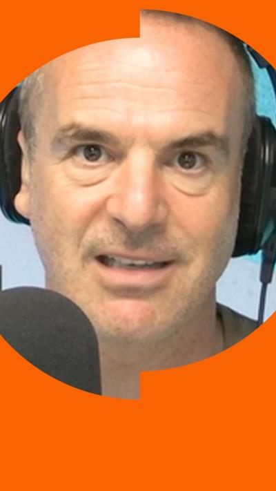 A man with short hair looks into the camera as he talks into a microphone