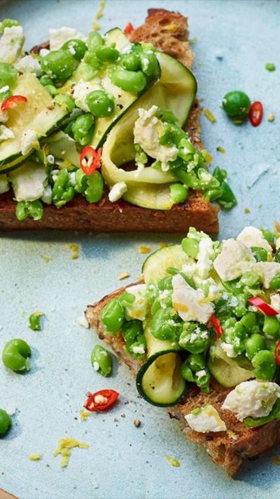 Courgettes, peas and feta on toast, sitting on a blue plate