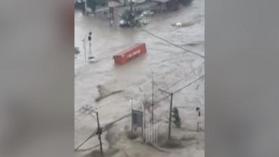 A shipping container floats down a flooded intersection.